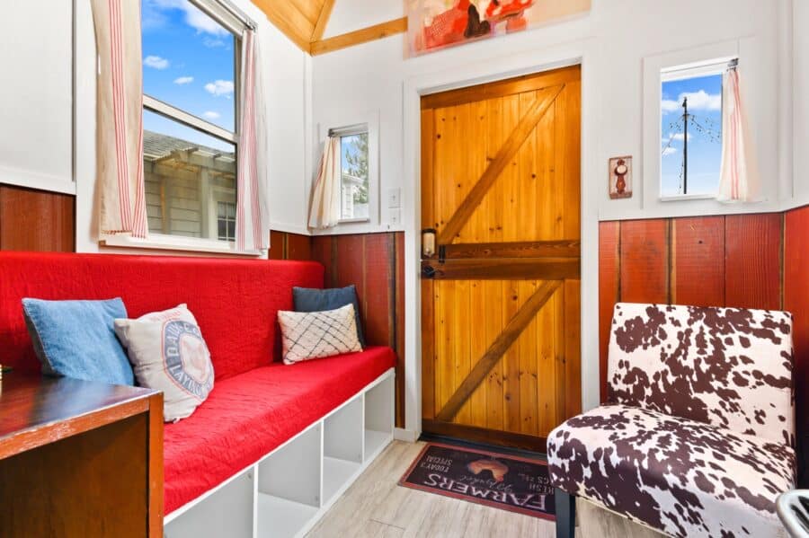 Red bench, cowhide chair, and Dutch door in the living area of the Barn tiny house