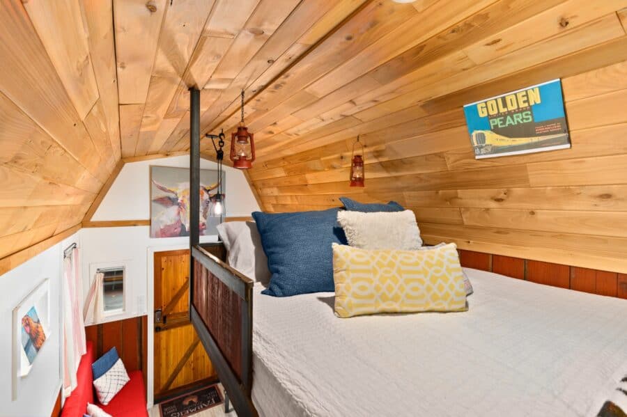 Queen bed in the wood-paneled gambrel roof loft of the Barn tiny house