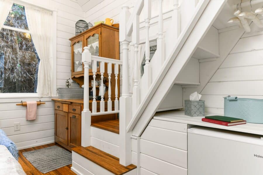 Antique hutch kitchenette and white staircase in the Cottage tiny house