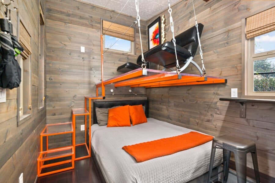 Queen bed under a clear suspended lounge loft with orange steel frame in the Modern tiny house