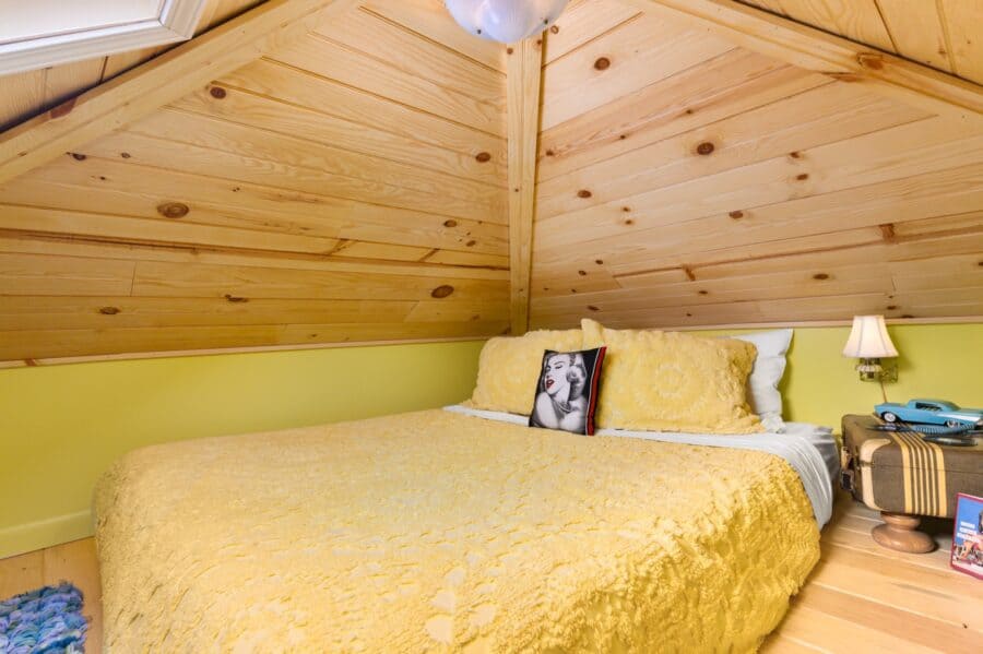 Queen bed under knotty pine in the skylit loft of the Rock n Roll tiny house