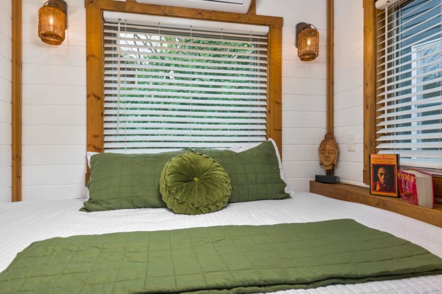 Queen bed with green linens beneath large windows in the Zen tiny house