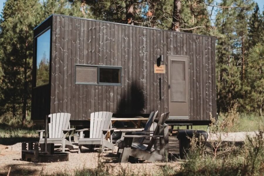 Charming tiny house cabin with dark wood exterior in a forest setting.