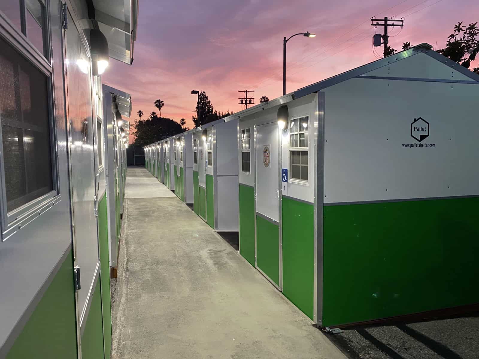A row of green and white Pallet tiny homes lit up at sunset with an ADA accessible unit marked at the end
