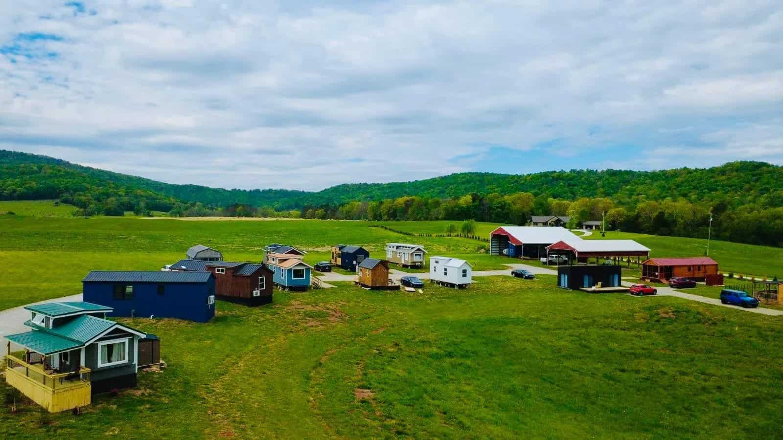 Wide view of Tiny Homes Village showing tiny homes, green pasture, and forested hills