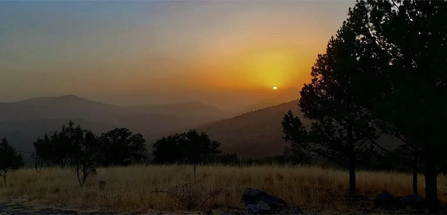 Sunset over a scenic Texas landscape with a tiny house in the distance.