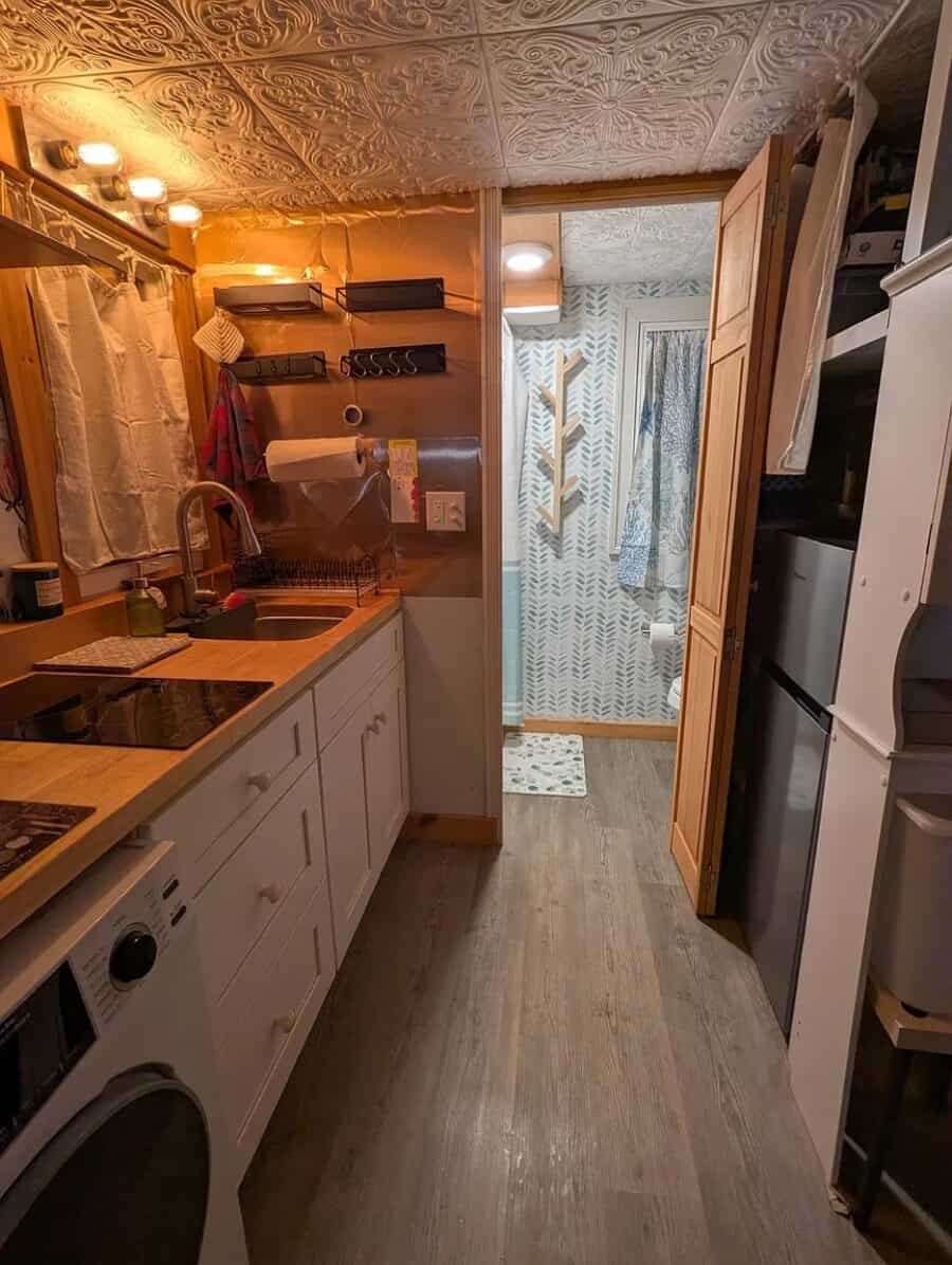 Compact tiny house kitchen with modern appliances and warm lighting.
