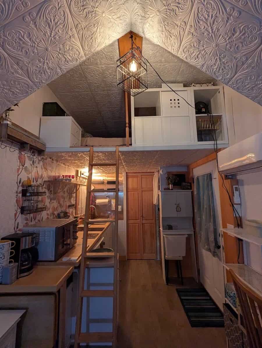 Interior of a tiny house with a loft bedroom and compact kitchen space.