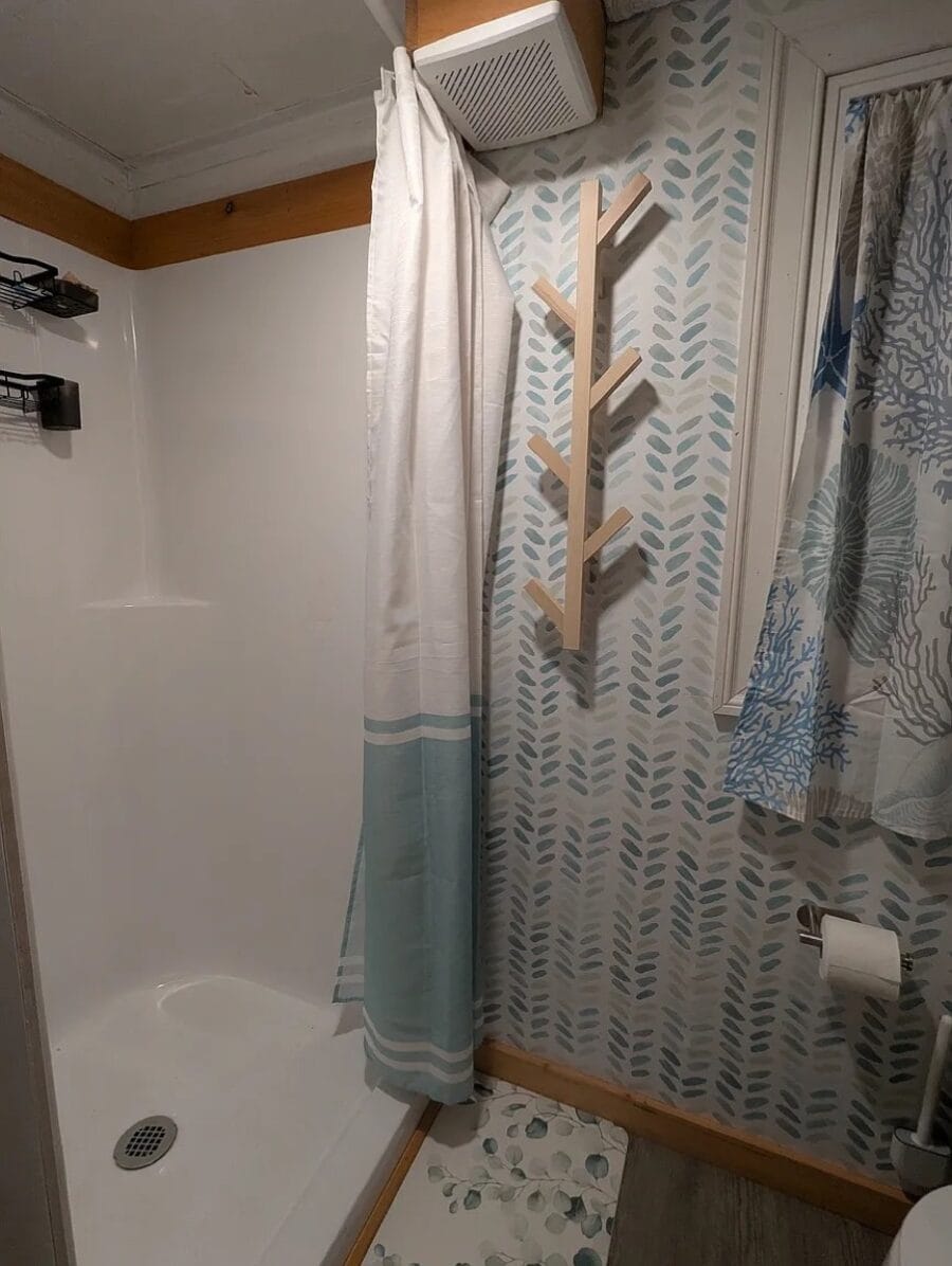 Compact bathroom featuring a wooden tree-shaped wall shelf and patterned wallpaper.