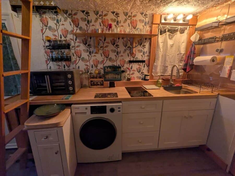 Compact tiny house kitchen with floral wallpaper and modern appliances.