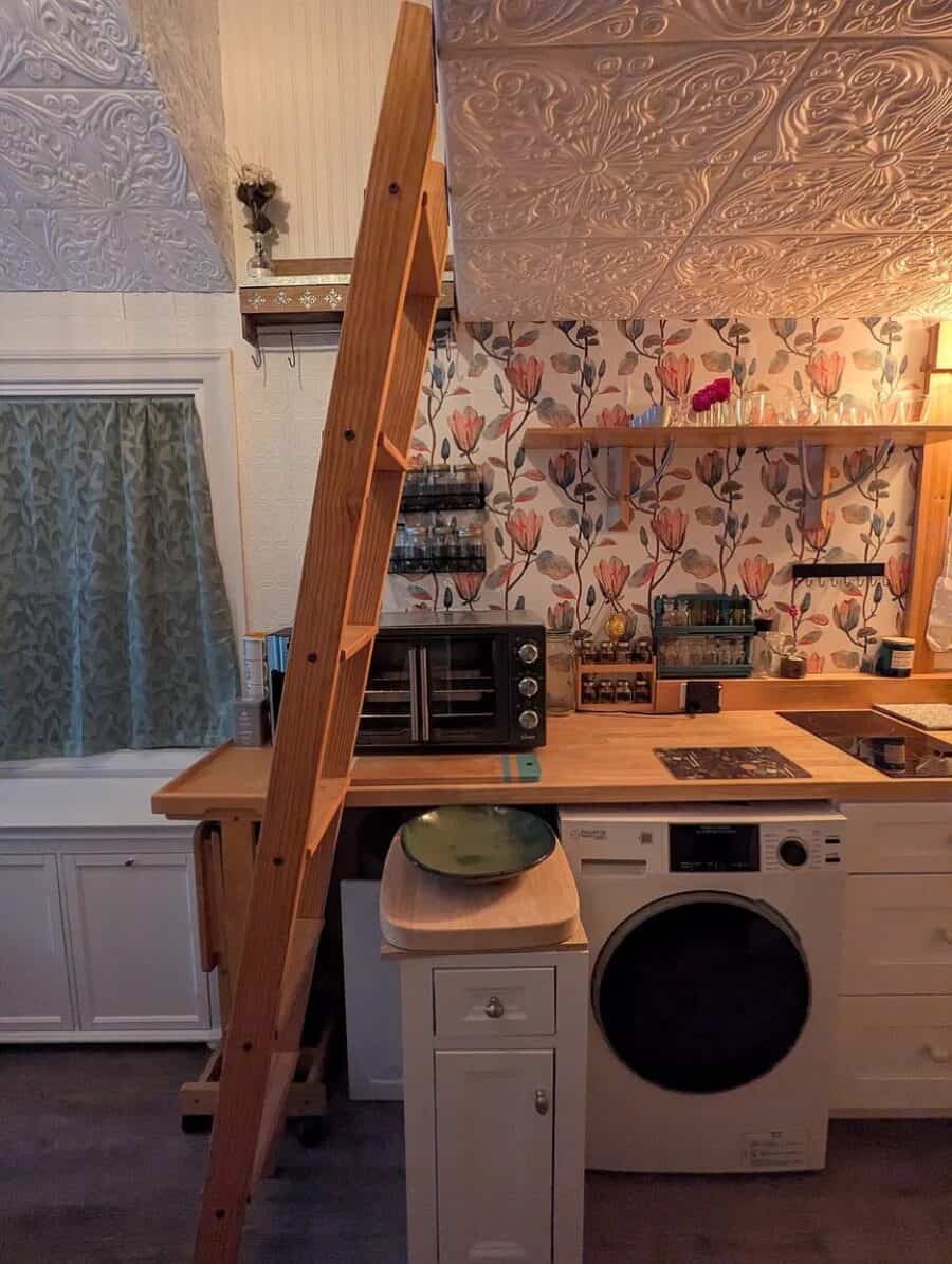 Interior of a tiny house kitchen with a loft, featuring a washing machine, oven, and decorative wall.
