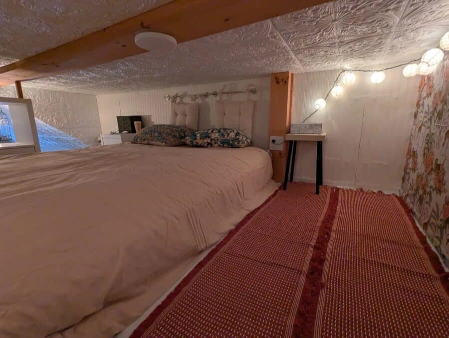 Compact bedroom in a tiny house with warm lighting and a sloped ceiling.