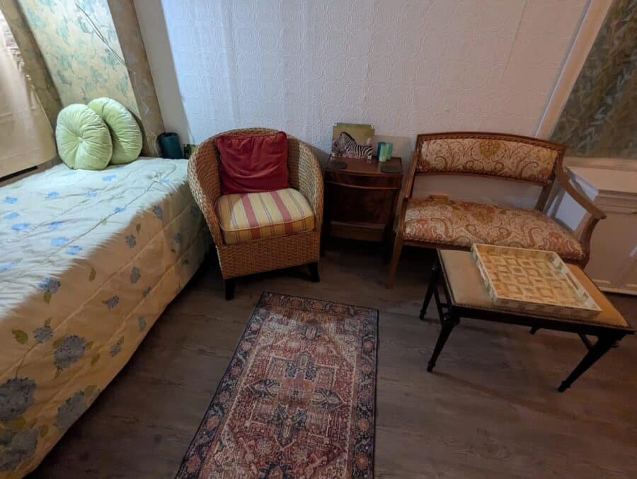 Cozy living space inside a tiny house with vintage furniture, a small rug, and a bed with floral bed.