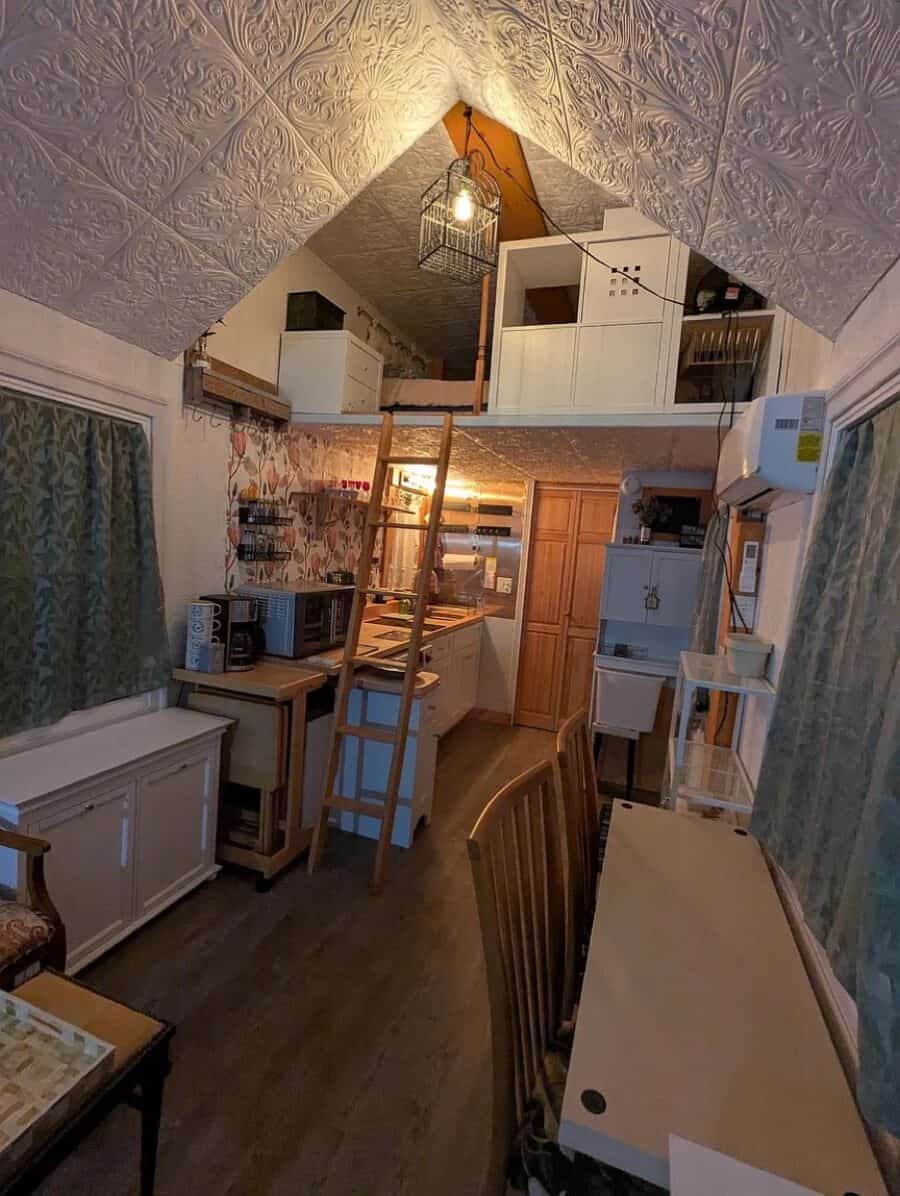 Interior view of a tiny house with loft, compact kitchen, and workspace.