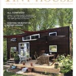Outdoor tiny house with deck, patio furniture, and lush trees in the background.