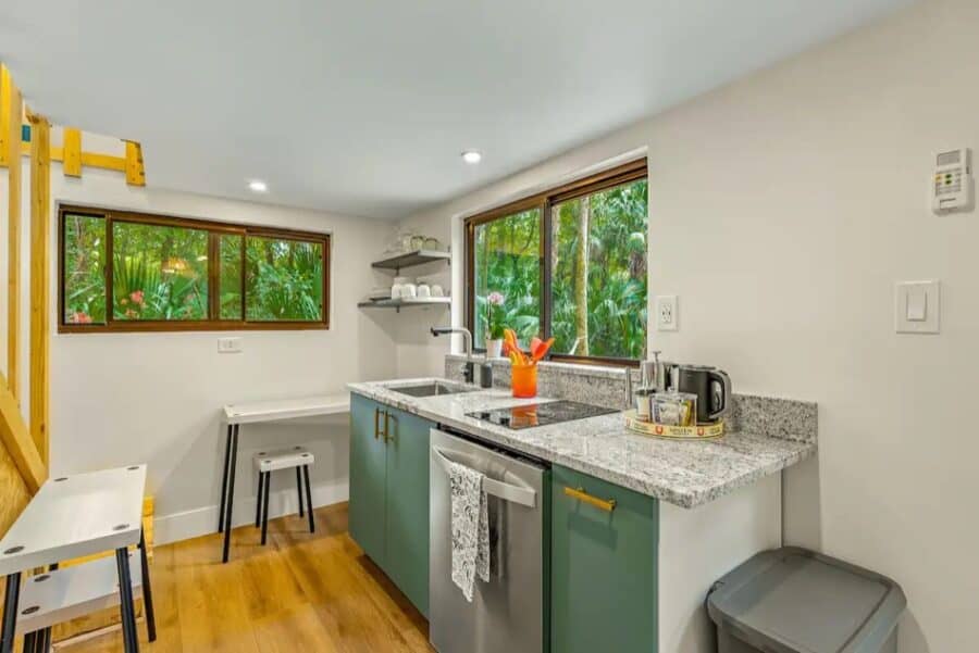 Bright tiny house kitchen with large windows overlooking lush greenery in Thonotosassa, Florida.