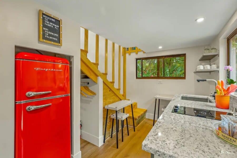 Charming tiny house interior featuring a vibrant red refrigerator, modern kitchen, and wooden stairc.