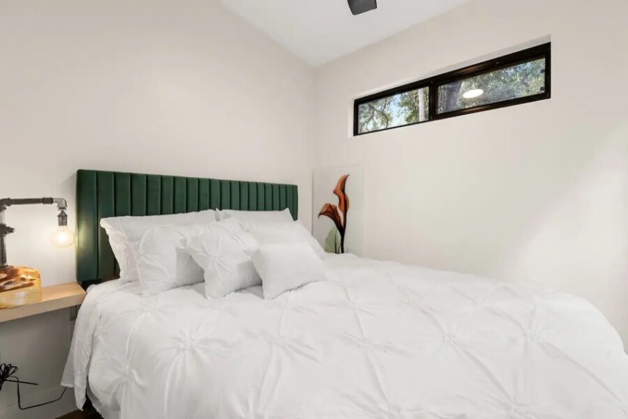 Bright tiny house bedroom with white bedding and a green headboard, large window, and minimalist des.
