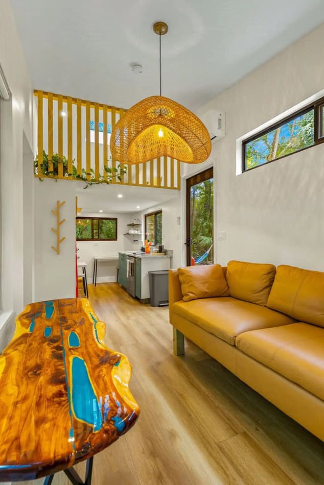 Bright tiny house interior with modern decor, wooden accents, and large windows in a forest setting.