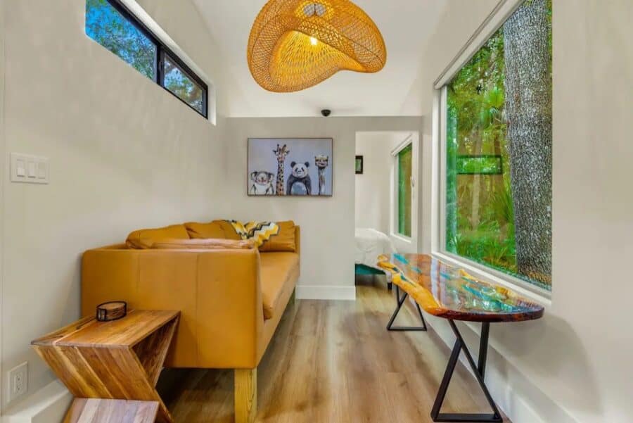 Bright tiny house interior with large windows showcasing lush forest views.