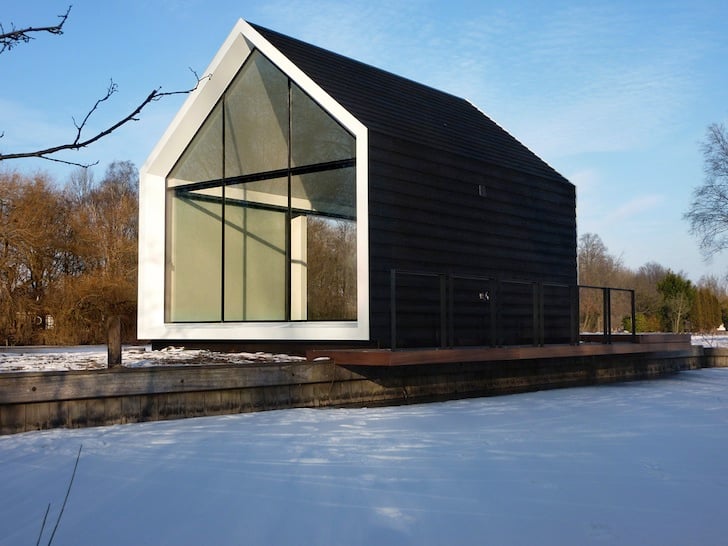 Winter view of the cabin from the frozen lake showing the dark cladding facade and jetty walkway