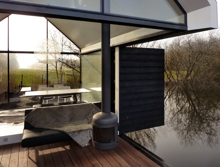 Folding wall open revealing the interior with wood stove and dining area, lake reflections on the terrace