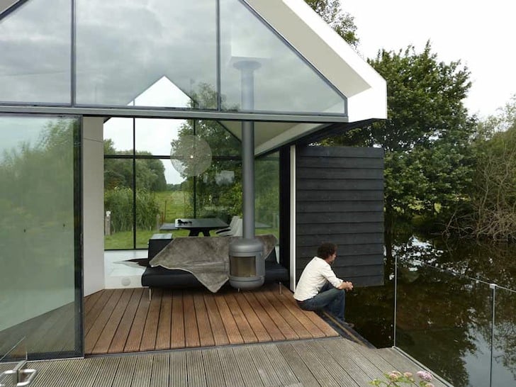 Person sitting on terrace edge by the lake with folding wall open showing the daybed and wood stove inside