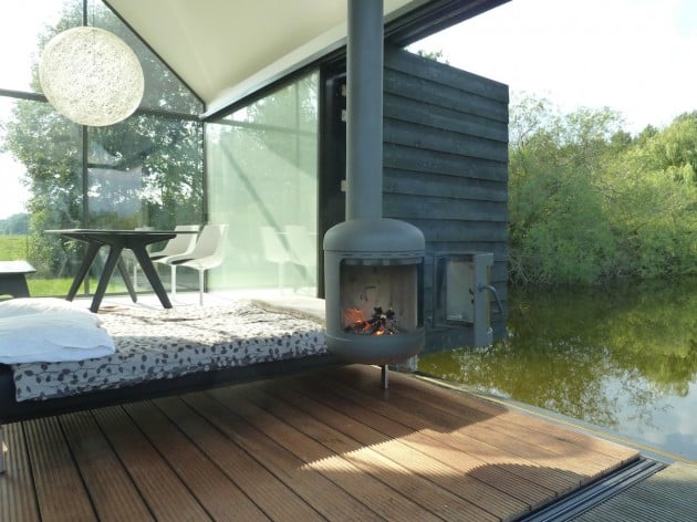 Interior showing daybed sleeping area, rotatable wood-burning stove with fire lit, sphere pendant light, and dining area in background