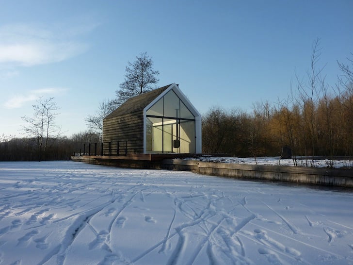 Wide winter shot of the cabin standing alone on the frozen lake with snow tracks leading to the entrance