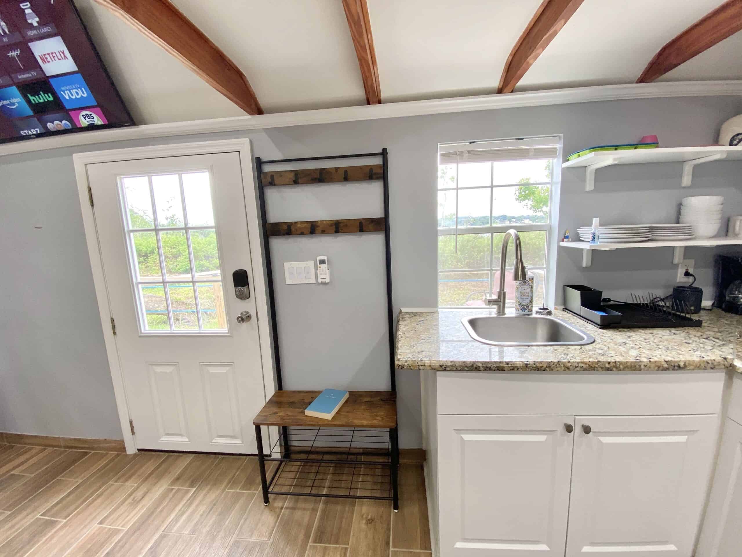 Entry door with coat rack, kitchen sink, and Smart TV visible in the tiny lake cottage