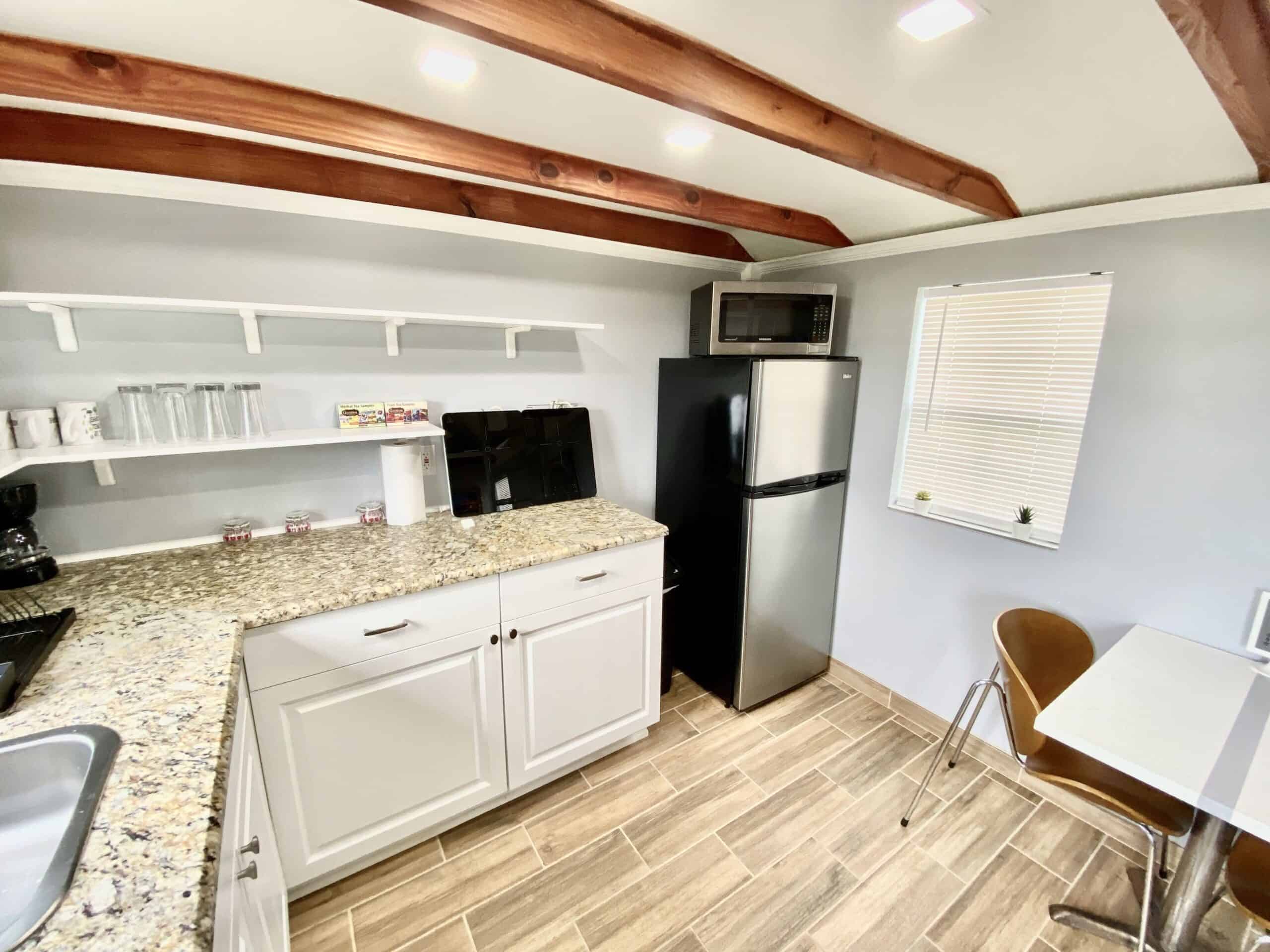 Kitchen with full-size fridge, stovetop, microwave, and open shelving in the tiny cottage
