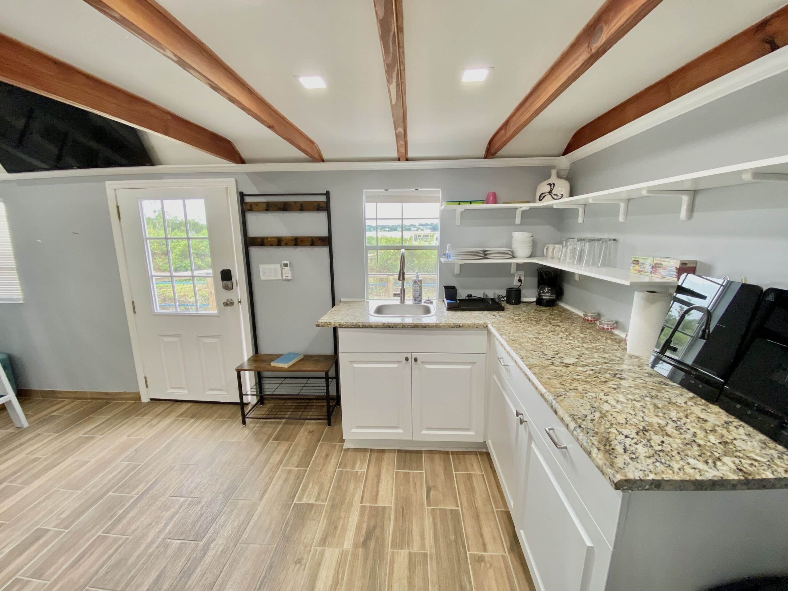 Tiny lake cottage kitchen with granite counters, white cabinets, and exposed wood beam ceiling