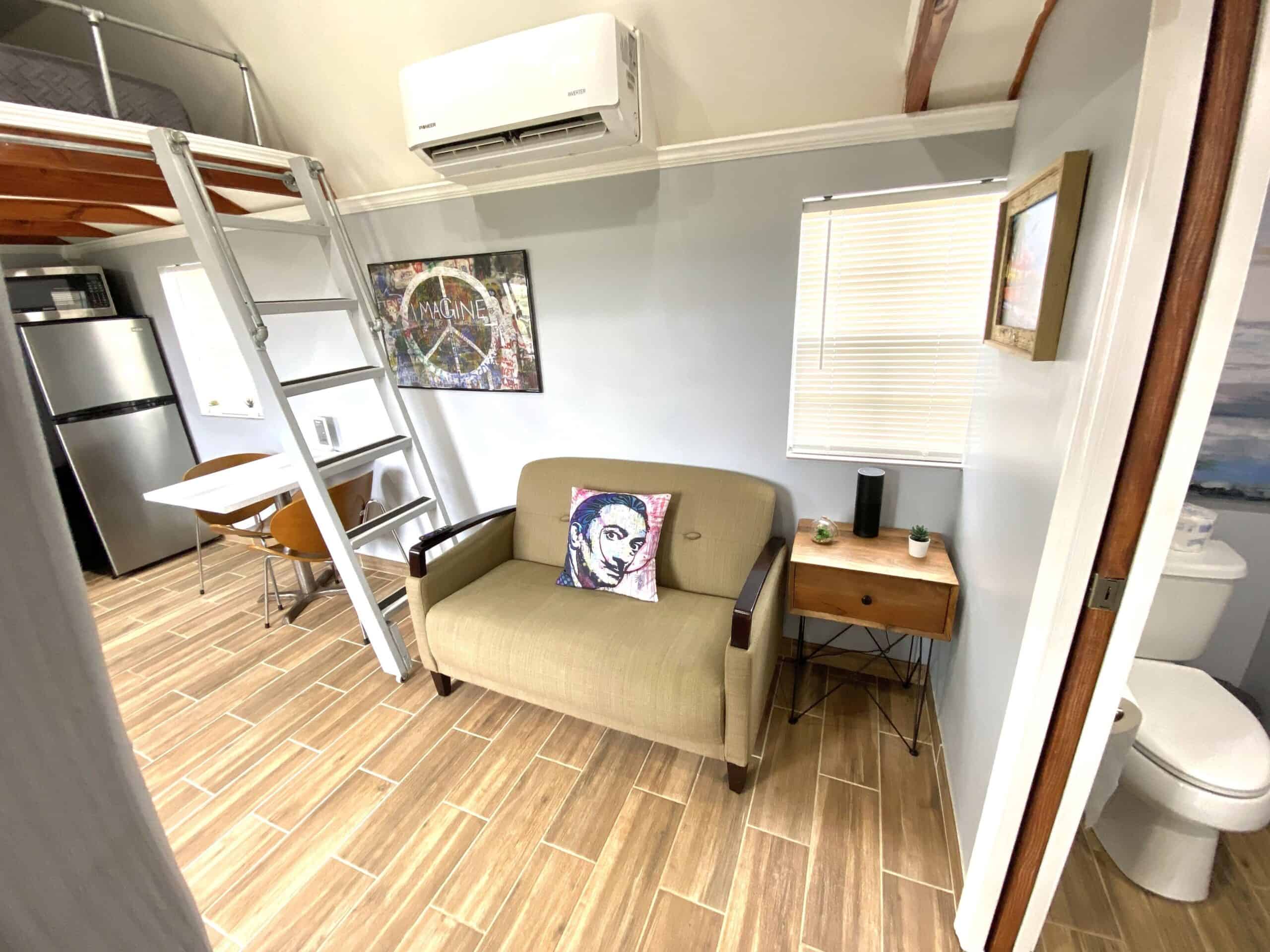 Living area with couch, loft ladder, art pillow, and mini-split AC in the tiny cottage
