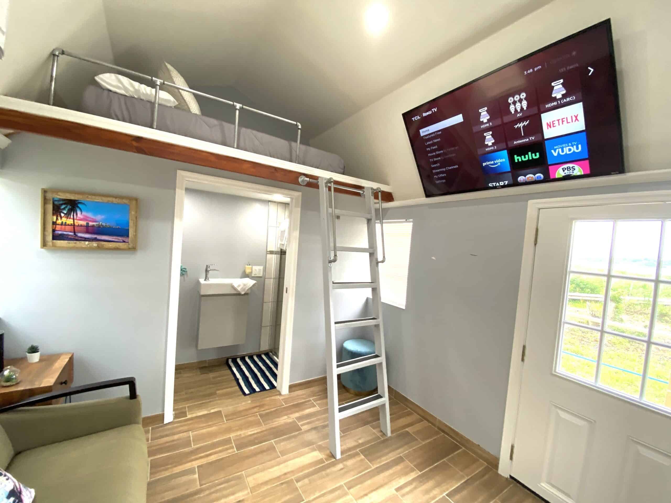 Loft bedroom with Smart TV and Roku streaming, ladder, and bathroom below in the tiny cottage