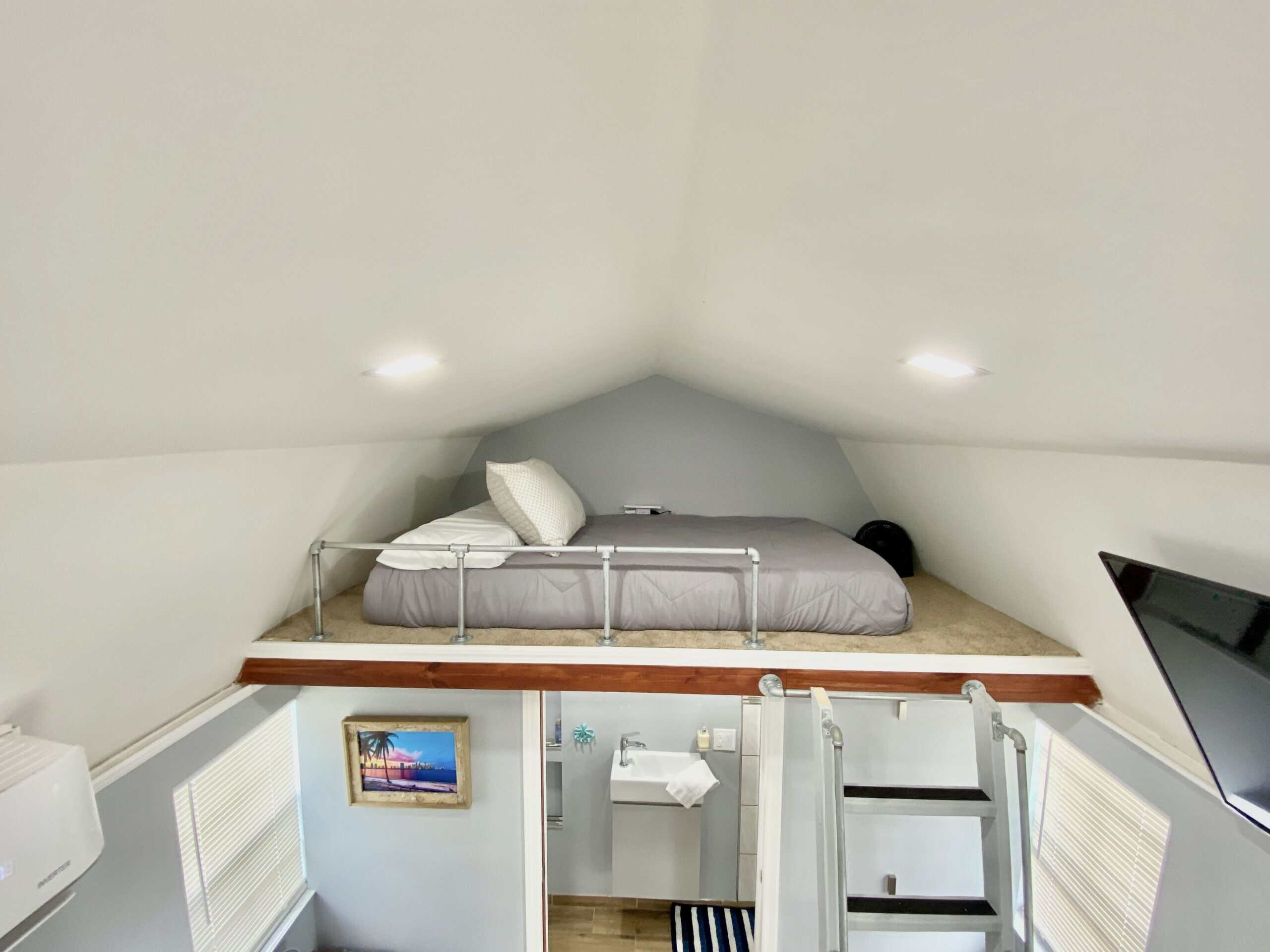 Loft bedroom under peaked roof with pipe railing and views down to the living space below