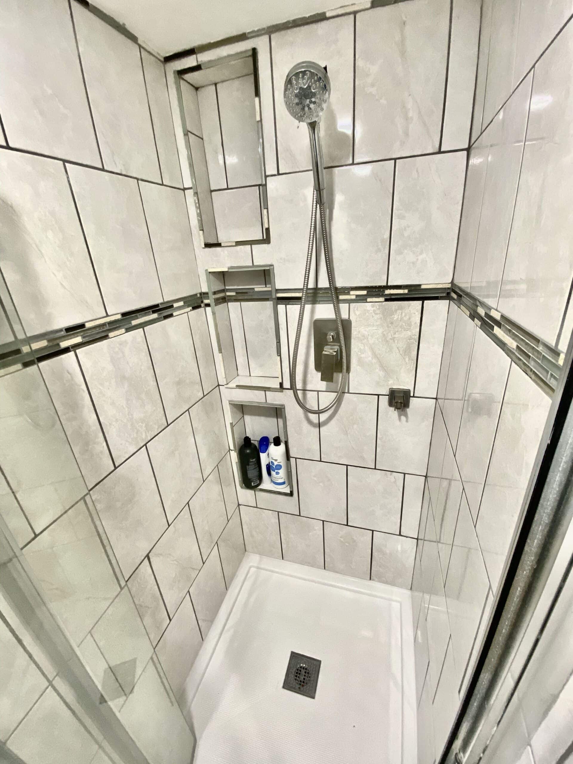 Shower detail showing tile niches and handheld showerhead in the tiny lake cottage