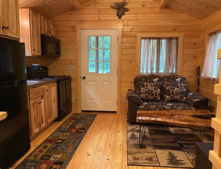 Charming tiny log cabin interior with wooden walls, small kitchen, and cozy seating area in Fort Whi.