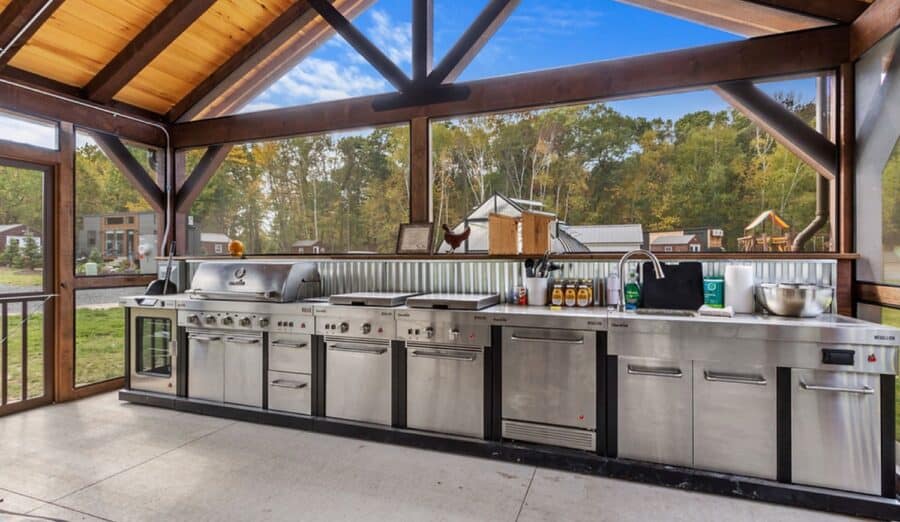 Modern tiny house kitchen with large windows and stainless steel appliances.