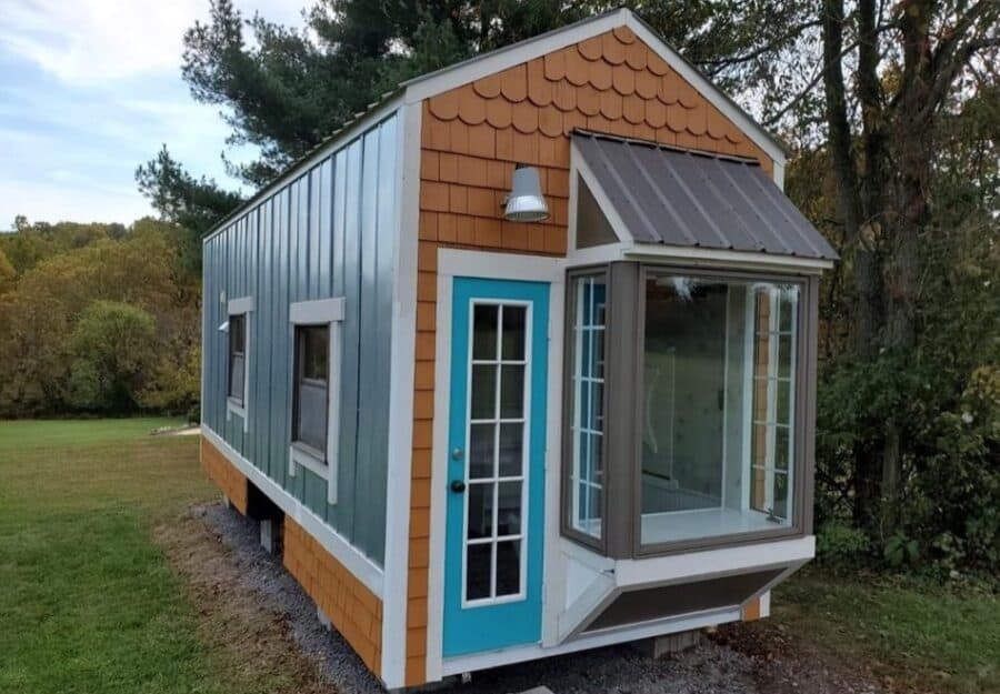 Tiny house with a blue door, bay window, and colorful exterior siding, set in a lush green outdoor e.