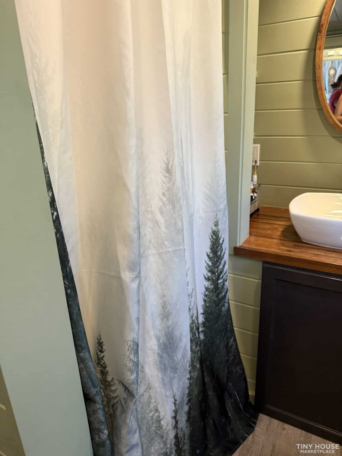 Bathroom with vessel sink on butcher block vanity, oval mirror, and forest shower curtain