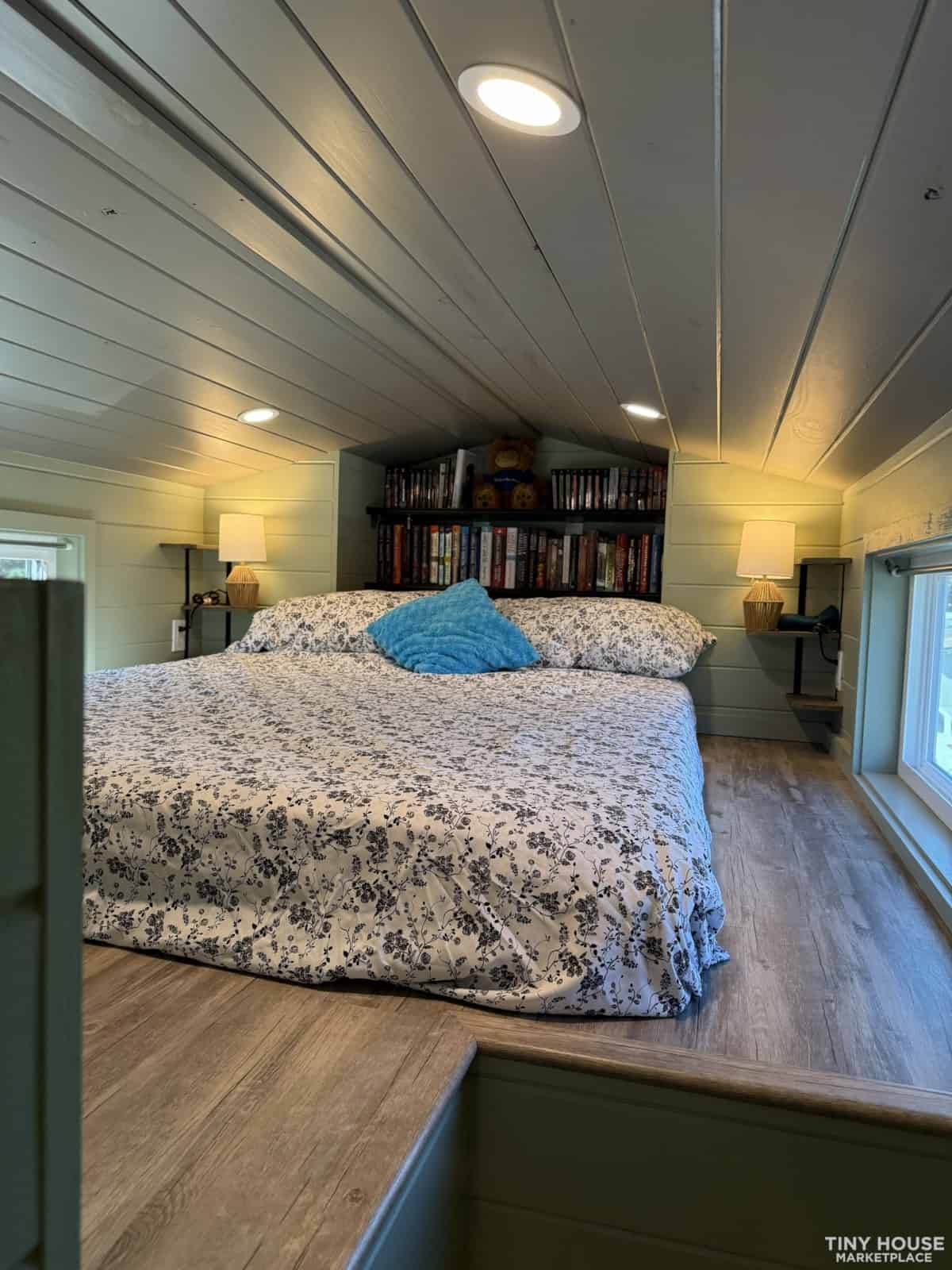 Spacious bedroom loft with queen bed, matching nightstand lamps, bookshelves, and large window