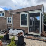 Charming tiny house featuring a compact, modern design with large windows and a cozy porch. Perfect.