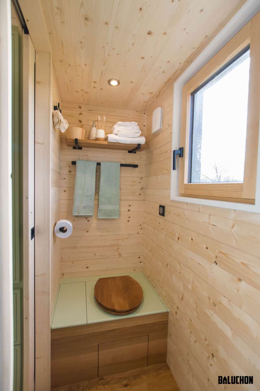 Compact tiny house bathroom with wooden interior and loft space.