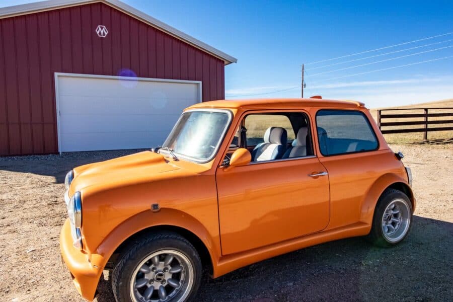 Vintage orange compact car in a rural setting with a red barn in the background.