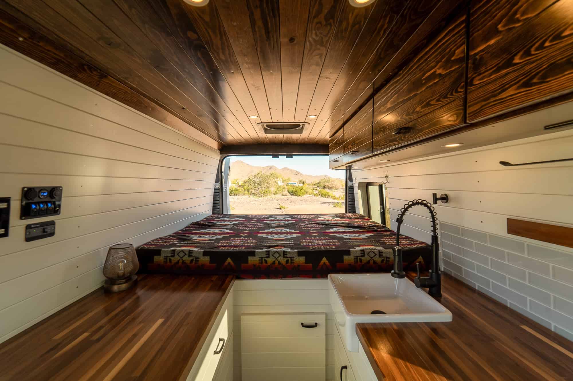 Fixed rear bed in the ProMaster camper van seen past the farmhouse sink and walnut counter