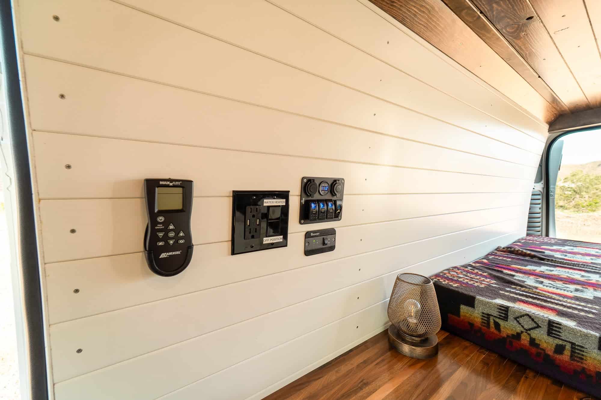 Wall-mounted control panel in the ProMaster camper van with MaxxAir fan controller, water heater switch and 12V switch panel