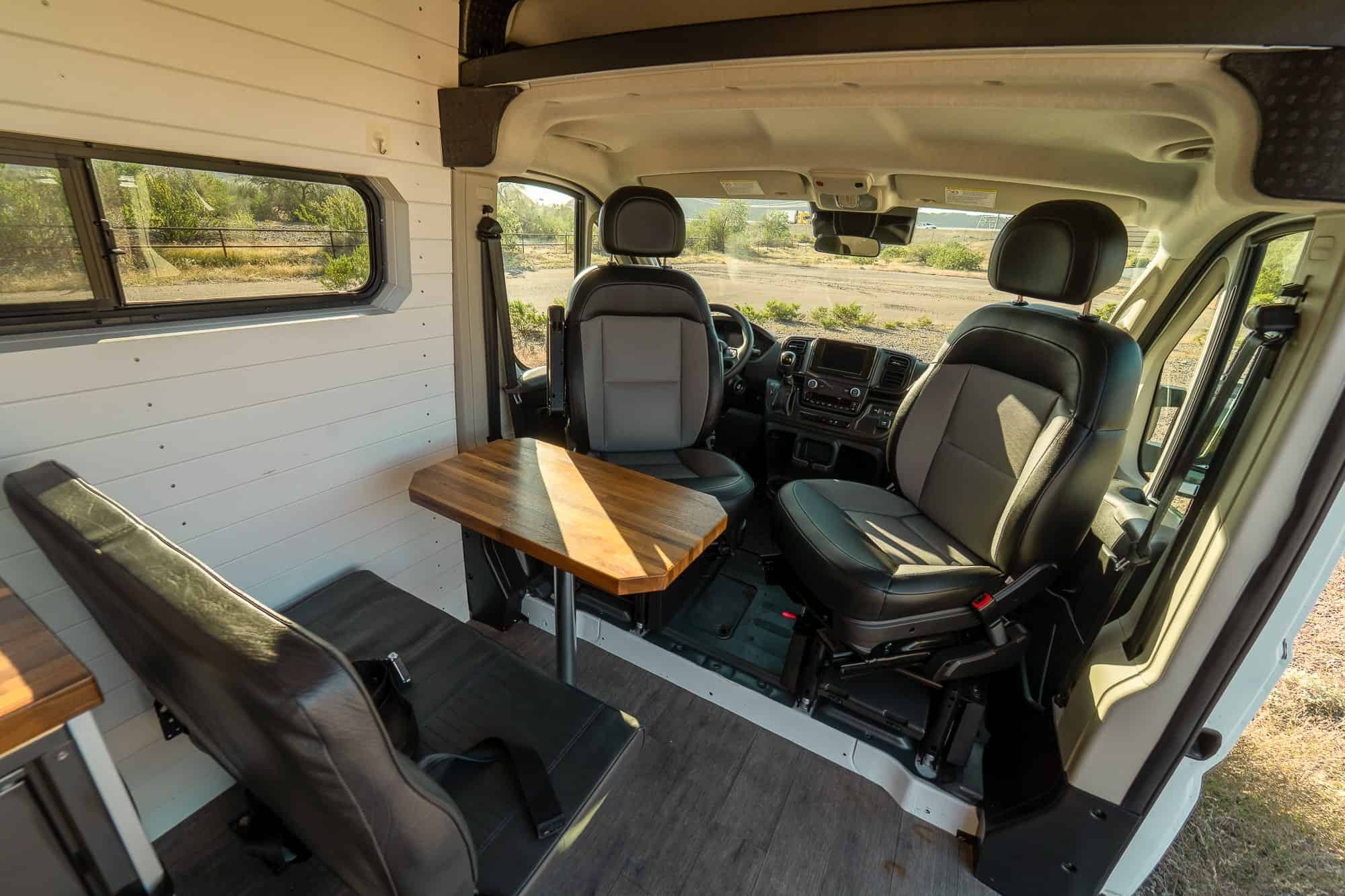 Walnut pedestal table and swiveling cab seats forming a dinette inside the Tommy Camper Vans ProMaster