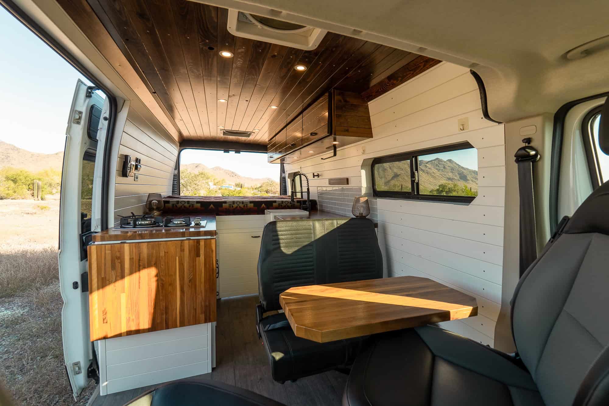 Interior of the Tommy Camper Vans ProMaster looking rearward with dark stained wood ceiling, white shiplap walls and walnut counters