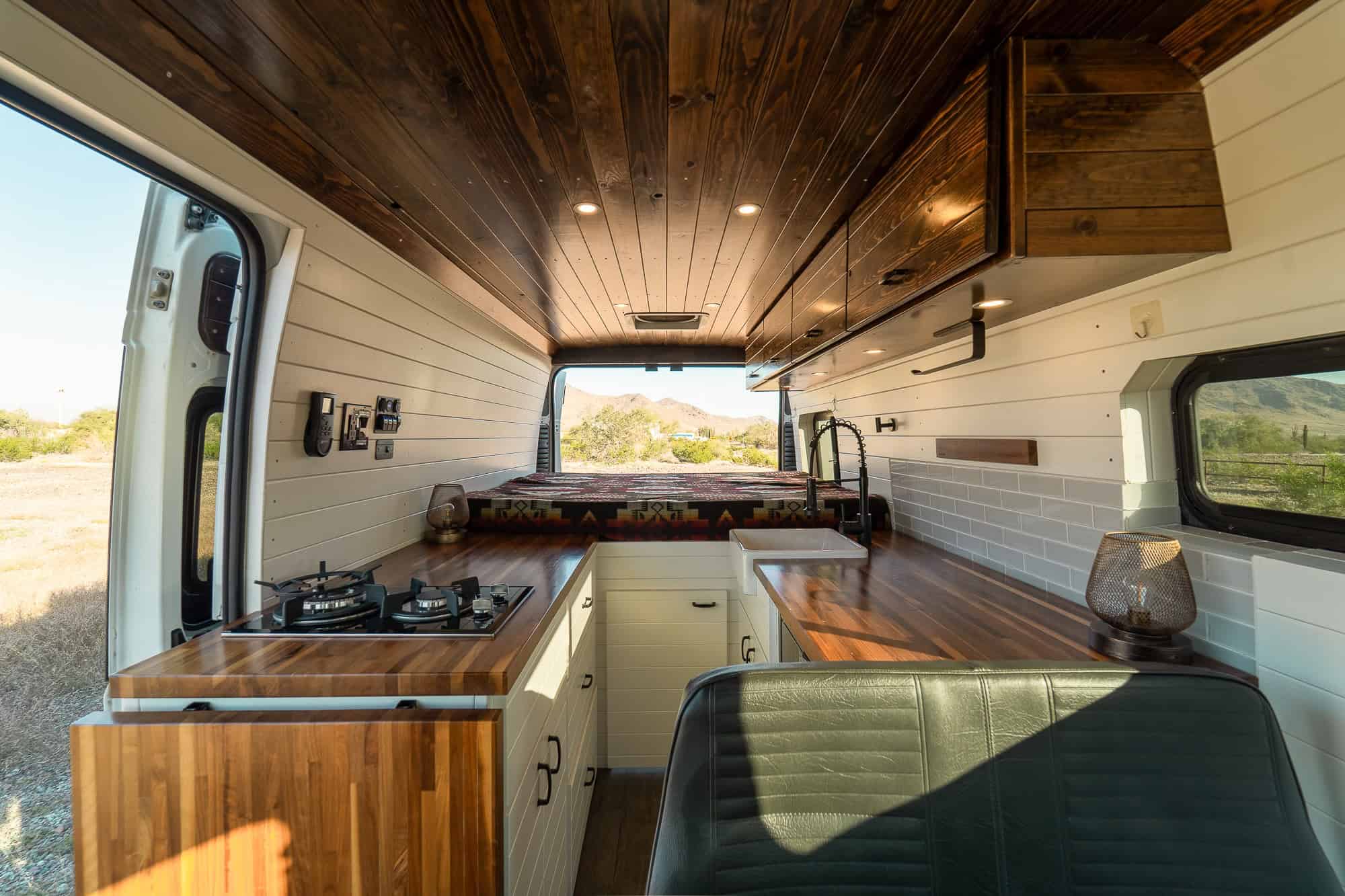 Wrap-around galley in the Tommy Camper Vans ProMaster with two-burner propane cooktop, walnut butcher block counters and farmhouse sink