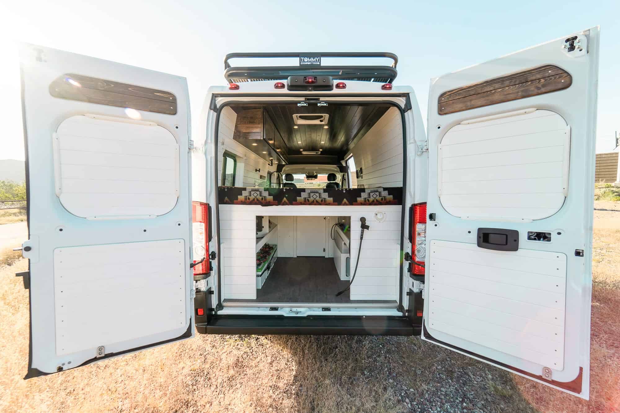 Rear doors open on the Tommy Camper Vans ProMaster showing the gear garage beneath the fixed bed